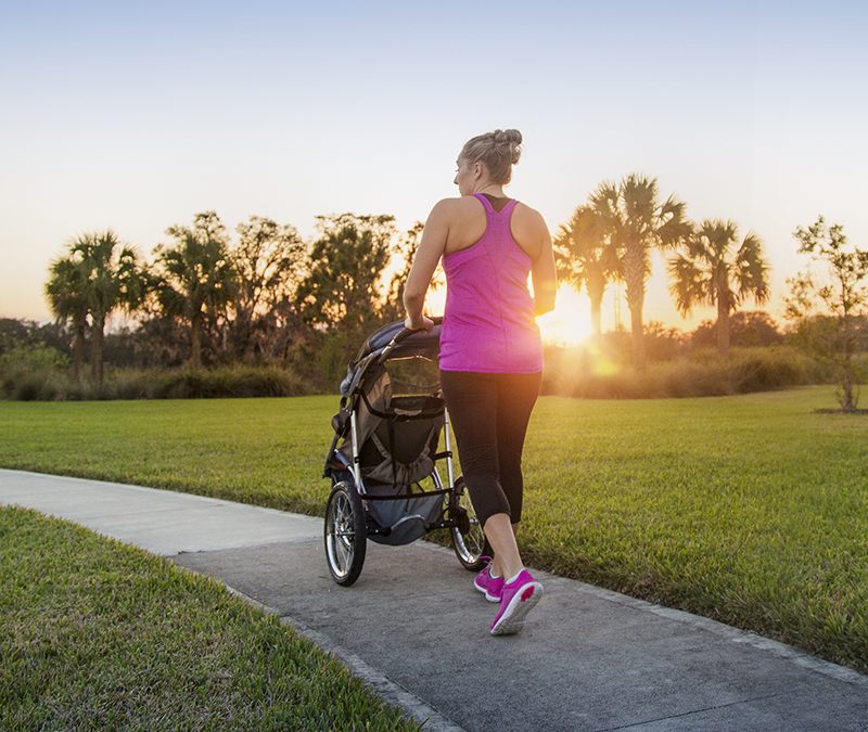a mother walking with a stroller through a park at sunset